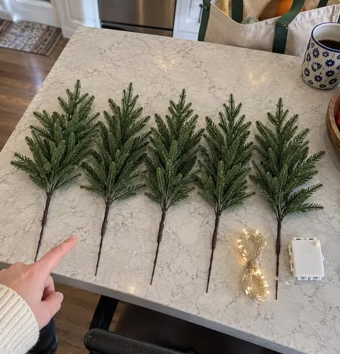 Five separate artificial pine stems and a coiled light string on a kitchen island