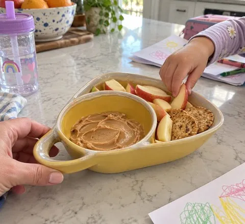 Yellow divided ceramic bowl serving fruit, crackers, and dip for a family snack