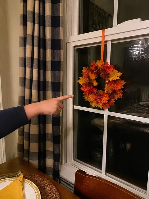 Maple leaf wreath hanging by a dining-room window before Thanksgiving dinner