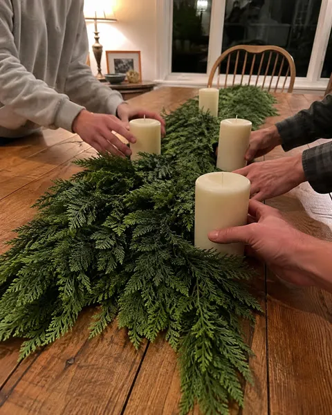 Family arranging cedar garland and candles on a dining table
