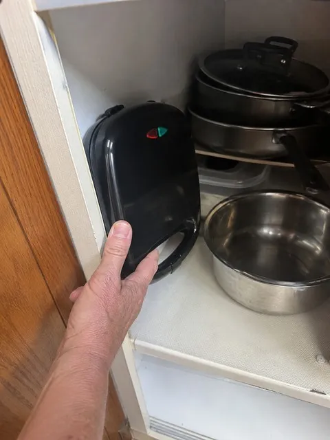 Compact waffle maker stored upright in a kitchen cabinet