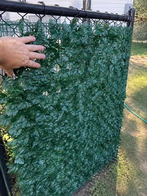 Deep green artificial ivy privacy screen secured to a backyard chain-link fence