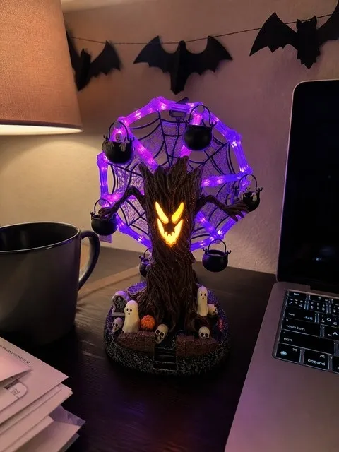 Haunted tree Ferris wheel glowing beside a laptop on a home-office desk