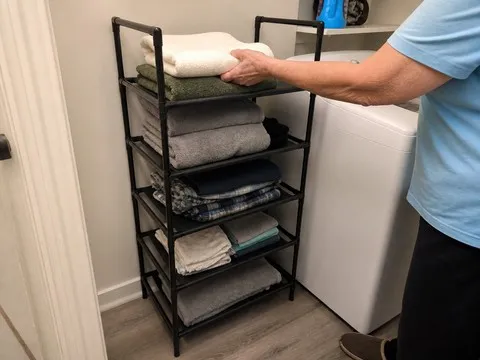 Five-tier rack holding towels and folded laundry beside a washer