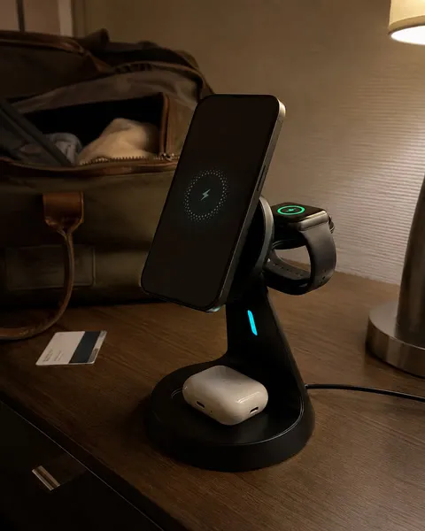 Black charging stand on a guest-room dresser beside a weekend bag