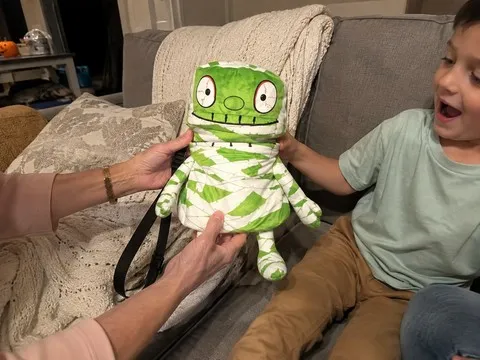 Child receiving a playful mummy crossbody treat bag at home