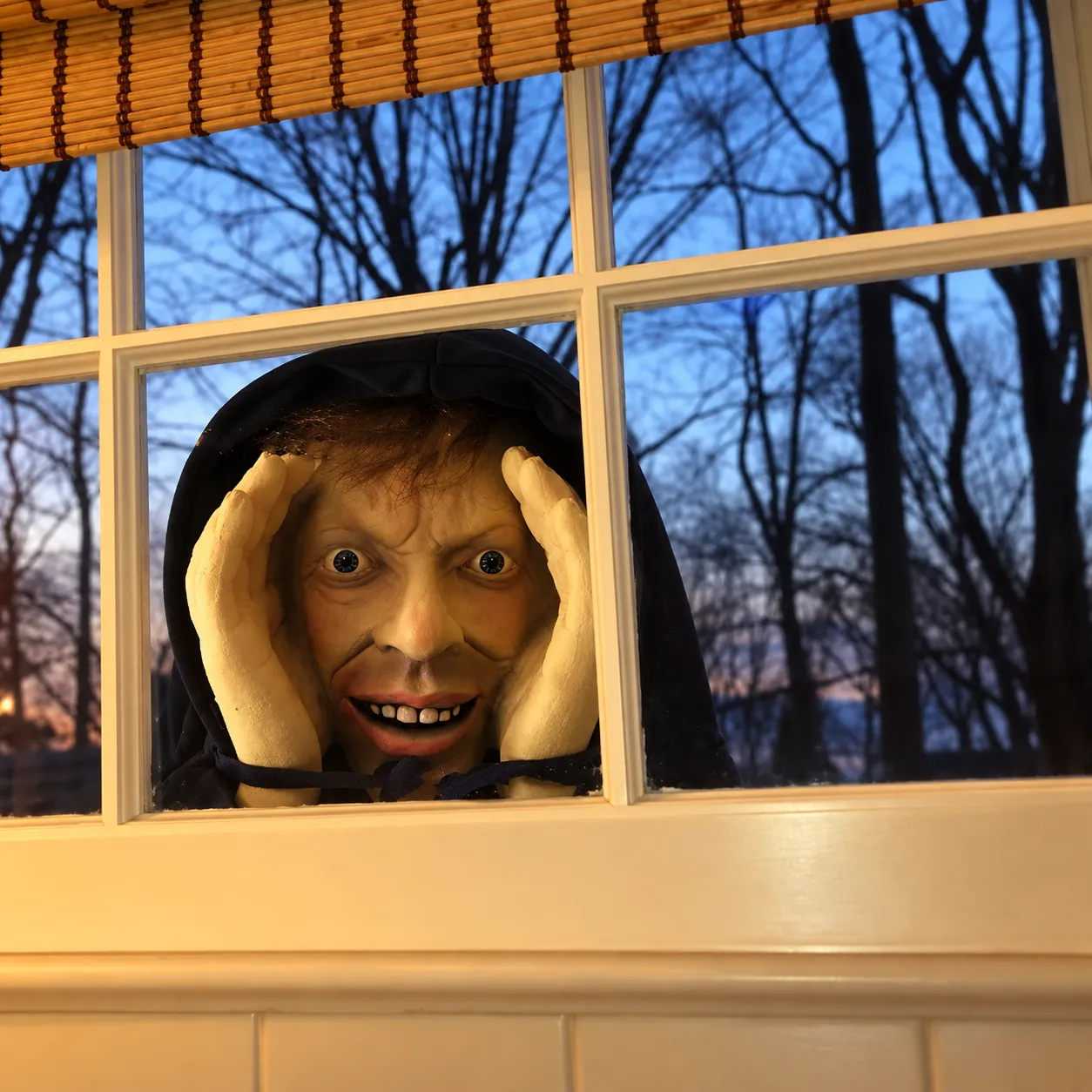 Creepy peeping face decoration outside a window at dusk