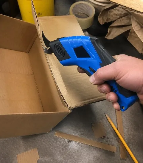 Cordless electric scissors used on cardboard in a garage