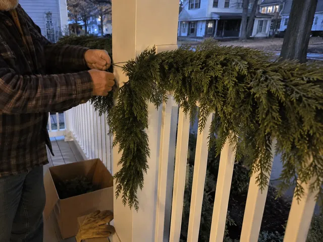 Garland being secured to a covered porch railing