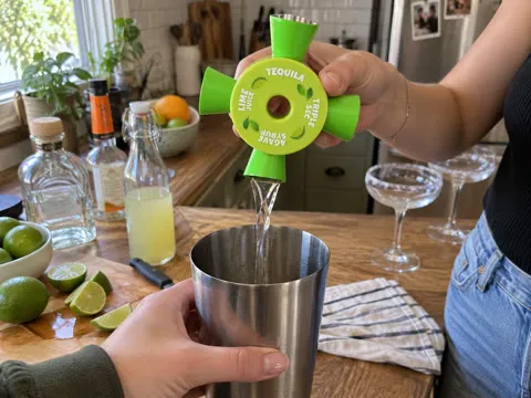 Friends using a green four-way cocktail jigger over a metal shaker