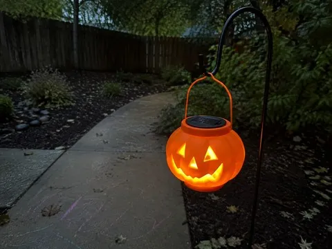 Glowing pumpkin lantern beside a backyard garden path at dusk