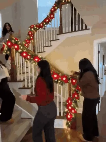 Pre-lit Christmas garland being arranged on a staircase railing