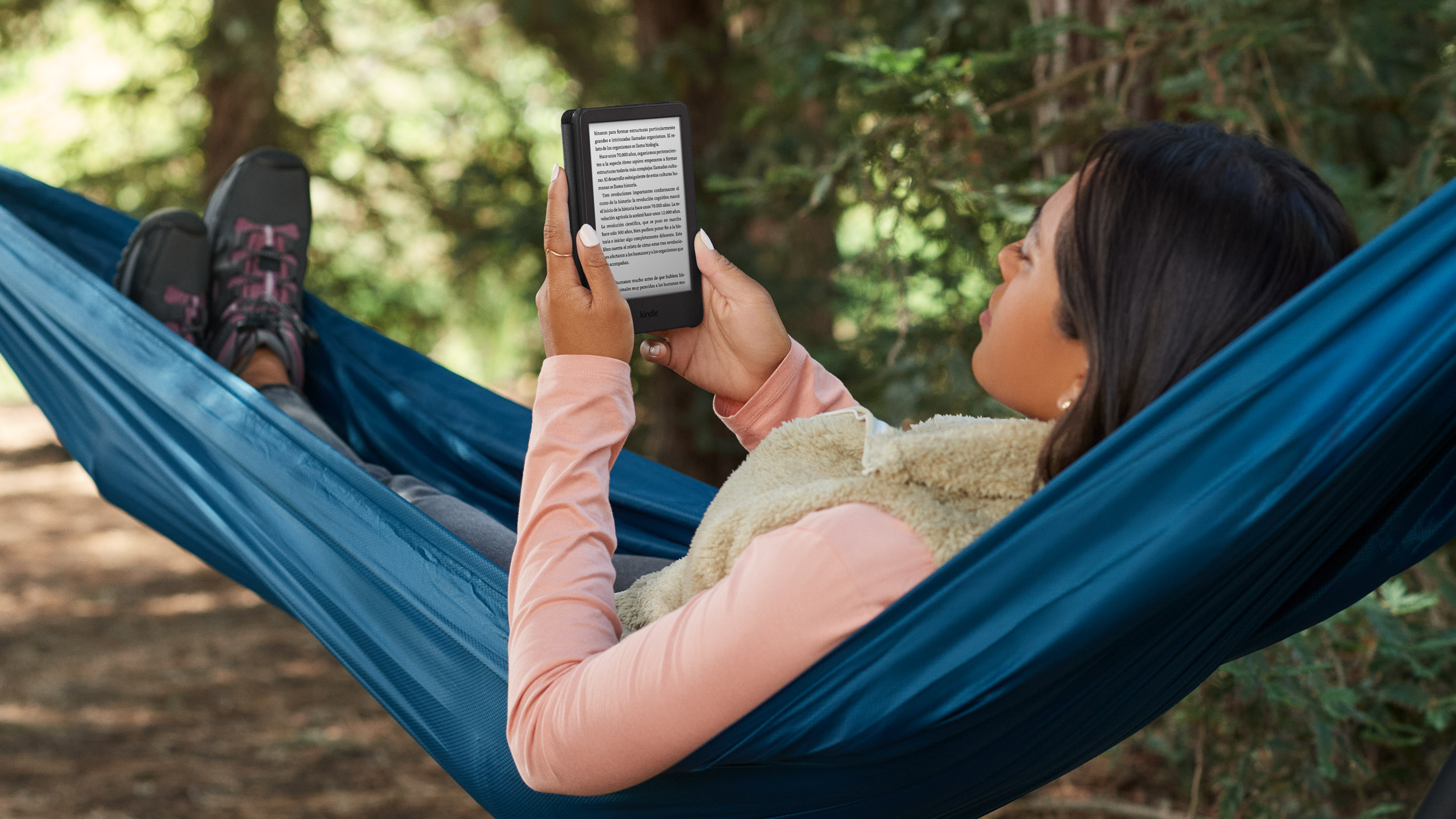 Mujer leyendo en un Kindle mientras est&aacute; acostada en una hamaca afuera.