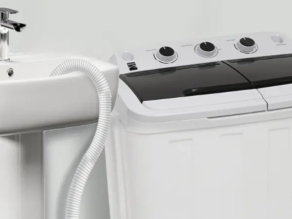 Closeup of Kenmore twin tub washing machine with drain hose hooked over the edge of a pedestal sink.
