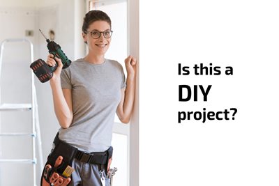 Woman holding drill leaning on wall asking if installing a SafeRacks overhead garage storage rack is a DIY project