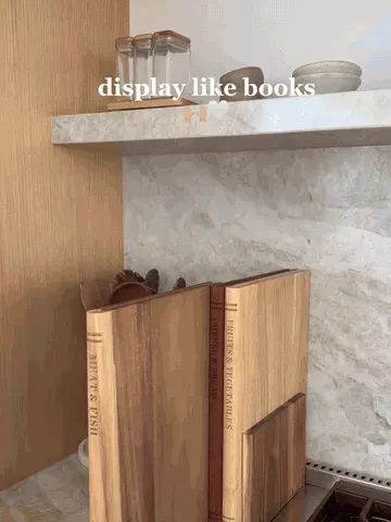 Three book-style solid wood cutting boards being selected from their upright stand