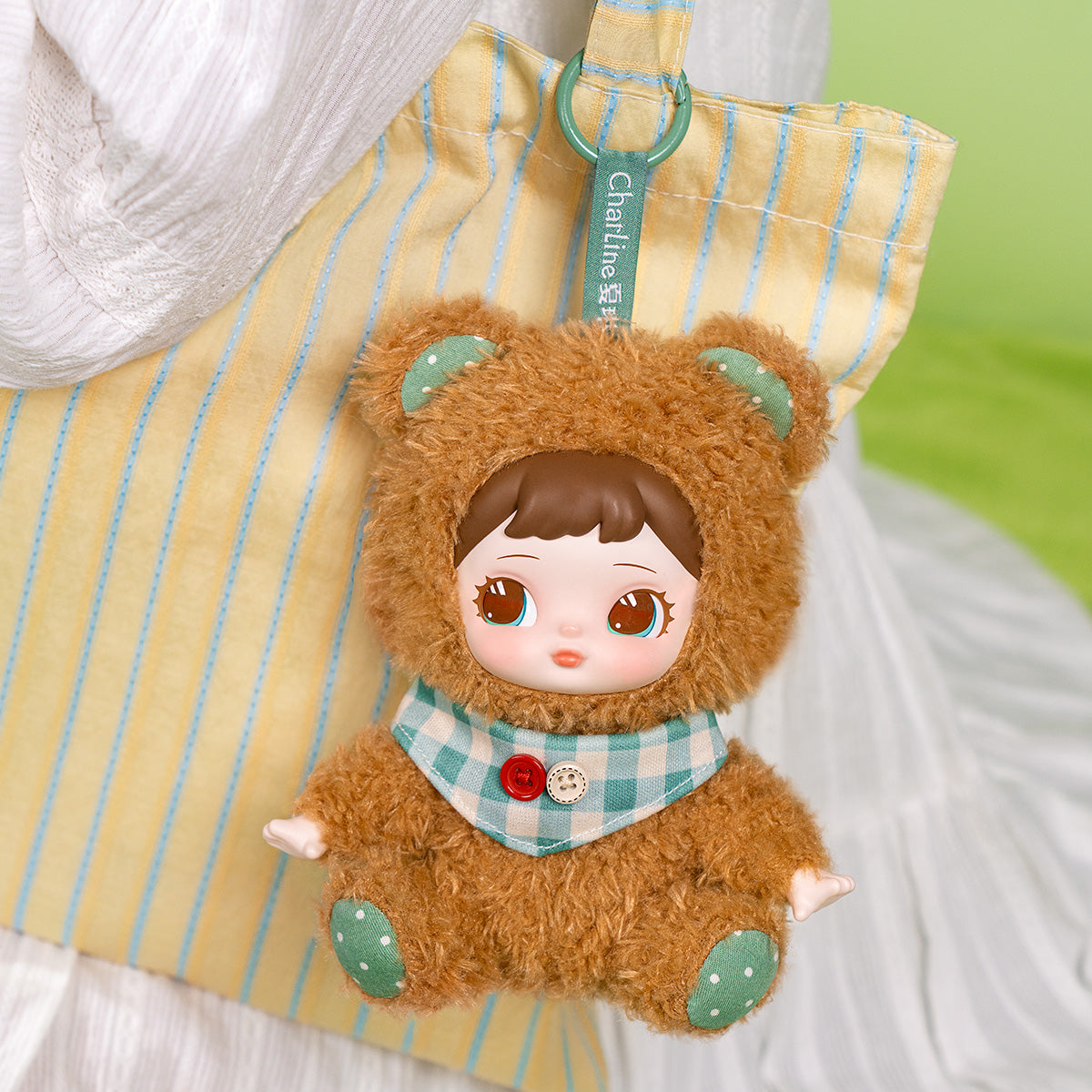 Charline Forest Hide and Seek Coco Bear pendentif en peluche accroché sur un tissu rayé