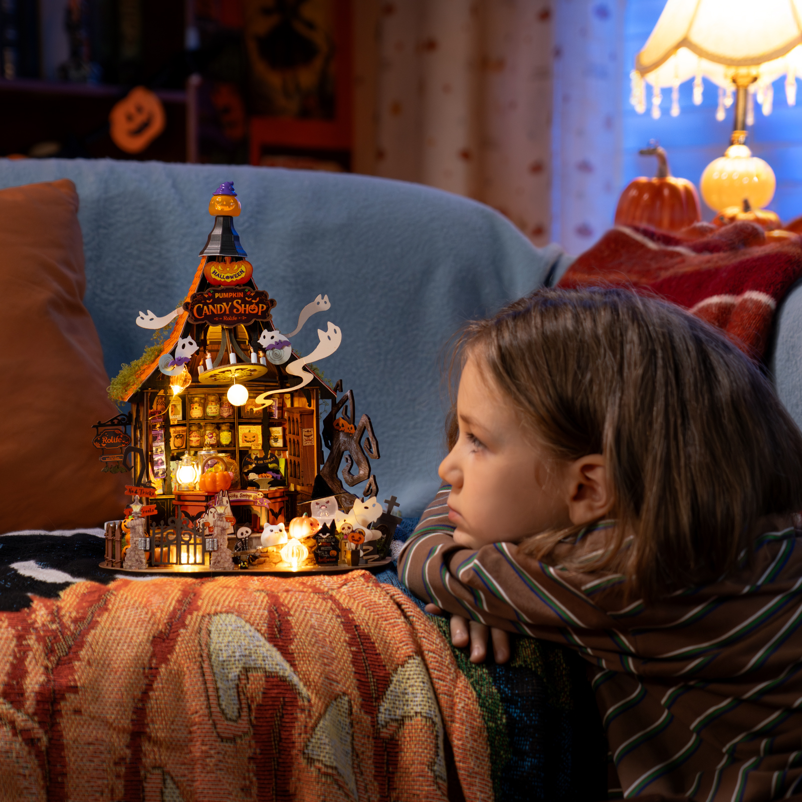 Kind kijkt naar de gloeiende Rolife Haunted Candy House-miniatuur in een gezellige Halloween-kamer