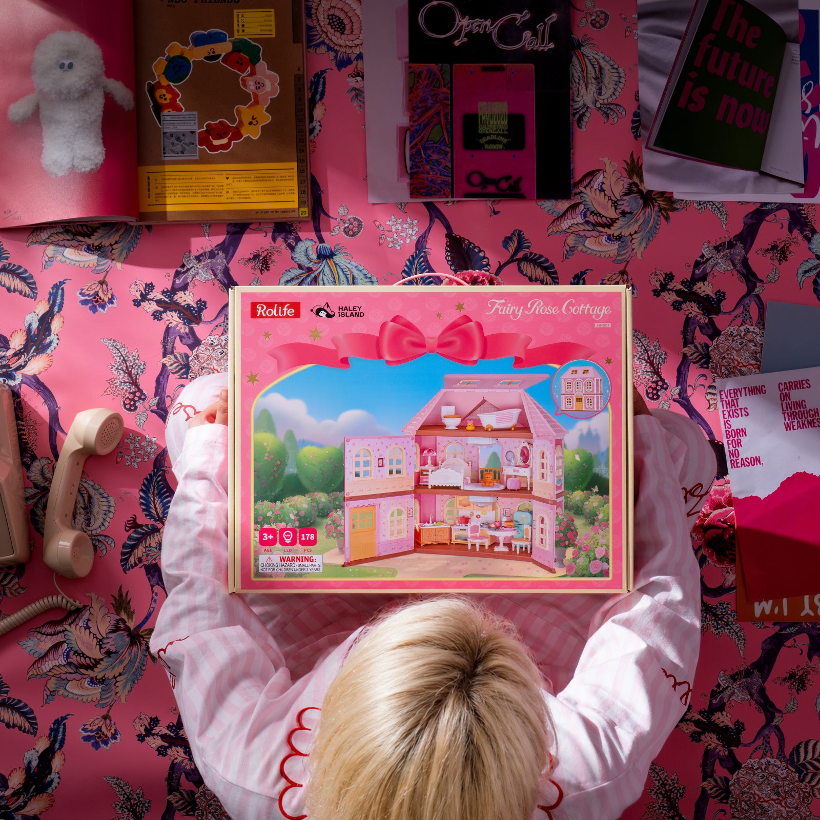 Rolife Fairy Rose Cottage HH001 El empaque del kit de bricolaje se muestra en una escena de habitación rosa.