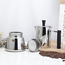 Stainless steel stovetop espresso maker set including pot, filter basket, and serving pitcher. Coffee beans and dried flowers in background.