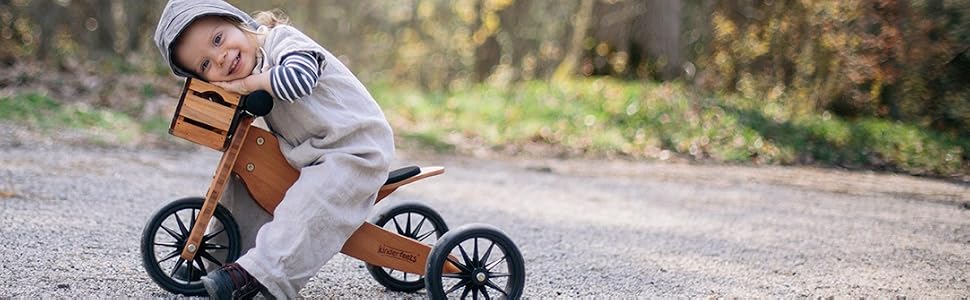 Kinderfeets balance bike natural wood black wheels child sitting forest background bike crate