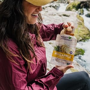 A woman is eating dried pineapple next to a river.