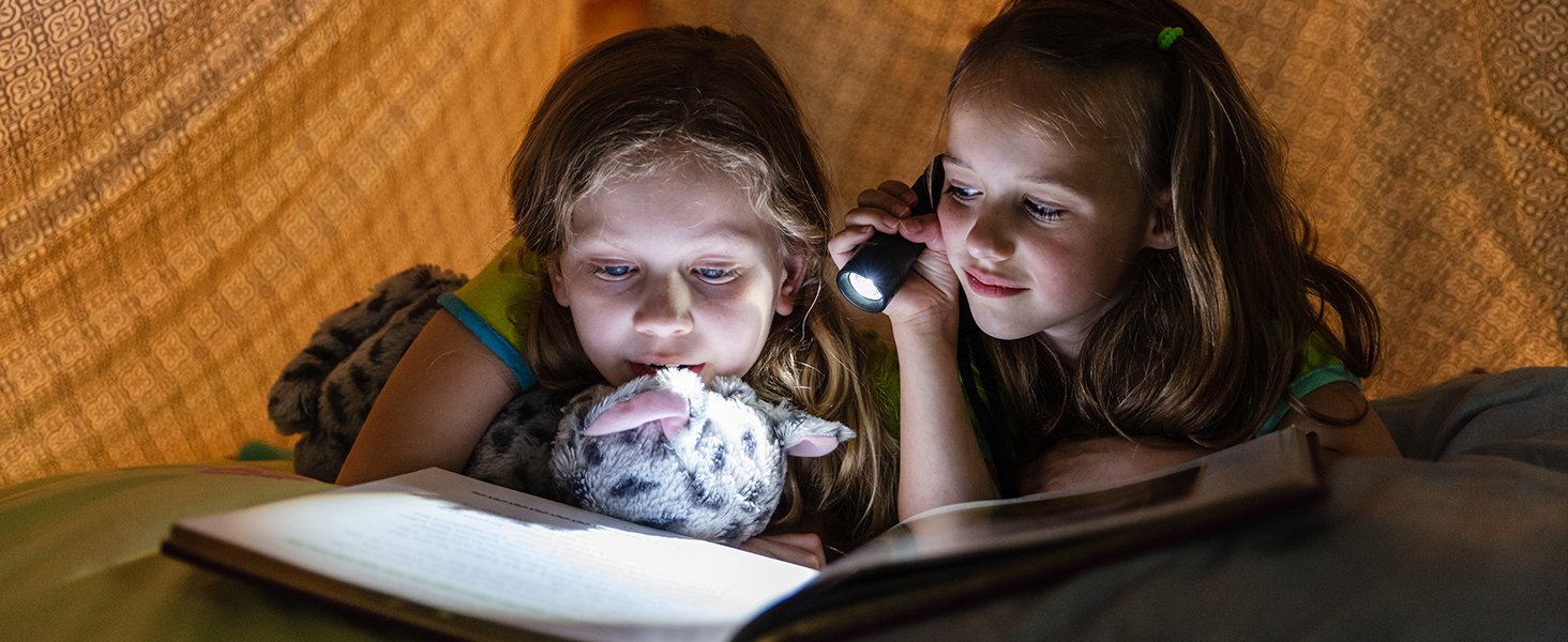 two young girls reading a book with a flashlight.