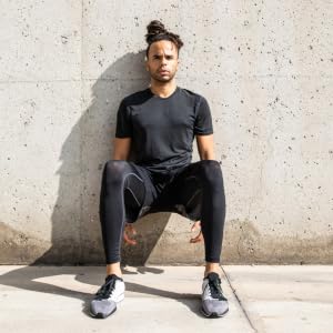 A man in a wall-sit position, with his back pressed against a concrete wall.