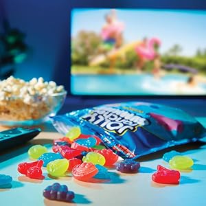 A bag of Jolly Rancher gummies candy spilling out near a bowl of popcorn in front of a television