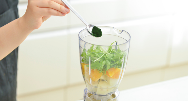 Adding Earthrise spirulina powder to a fruit smoothie.
