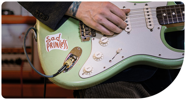 Mint green electric guitar with white pickguard and chrome hardware being played, showing pickups and control knobs.