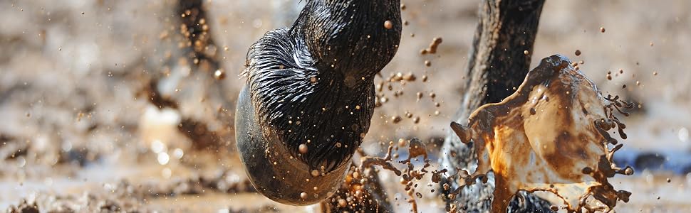 Close-up action shot of boots splashing in muddy water, capturing motion of mud and water droplets against dark background.