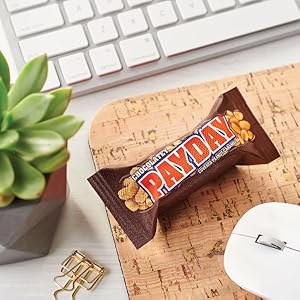 A snack size chocolatey Payday bar on a desk near a desk plant, keyboard and mouse