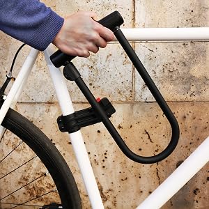 U-shaped black bicycle lock being attached to white bicycle frame, demonstrating secure locking mechanism.