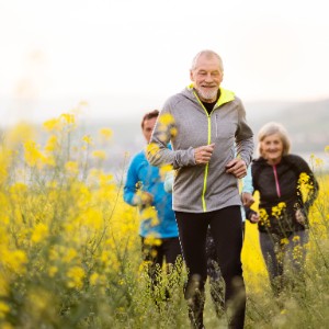 Senior man jogging in field with two runners trailing behind him
