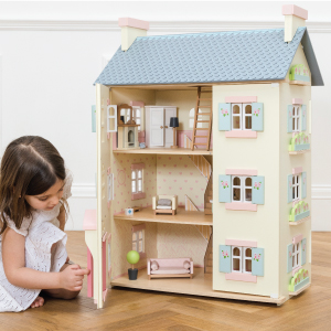 child opening large door on wooden dolls house showing furniture