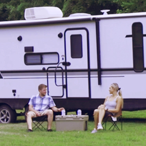 Couple in front of RV camping trailer enjoying drinks on a cooler