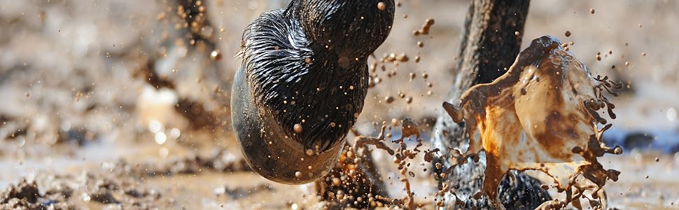Close-up action shot of boots splashing in muddy water, capturing motion of mud and water droplets against dark background.