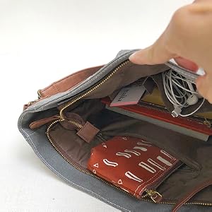 A hand holds open the MAIKA Crossbody bag to show many items in the interior pocket.