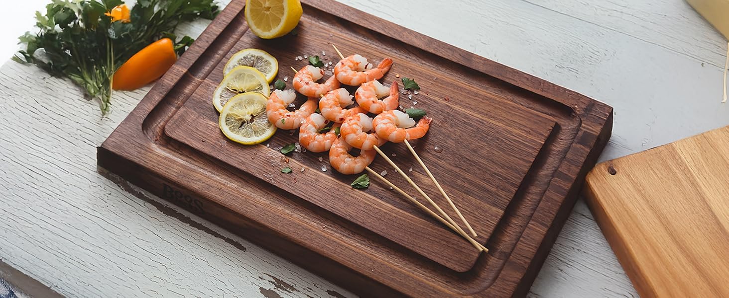 Walnut wooden board with shrimps on stick and lemons.