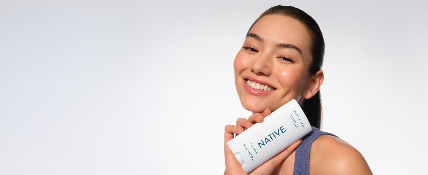 Smiling woman with fresh skin holds Native Sea Salt &amp;amp;amp; Cedar deodorant, looking confident.
