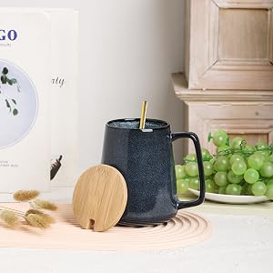 a black mug with a wooden handle and a wooden spoon on a table with grapes and a plate of grapes.