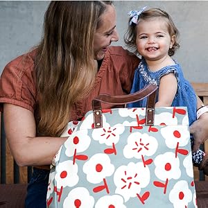 A woman holding a smiling toddler next to a MAIKA Carryall Tote in Sierra pattern.