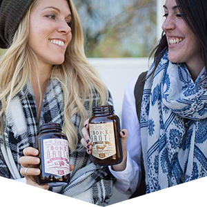 Two women smiling while each enjoy an EPIC gluten free bone broth beverage
