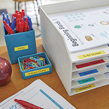 Desk with labeled filing tray and labeled pen holder with red and blue pens