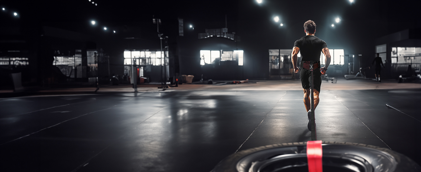Athlete sprinting across gym with sled pulling belt attached to tire for strength and speed training