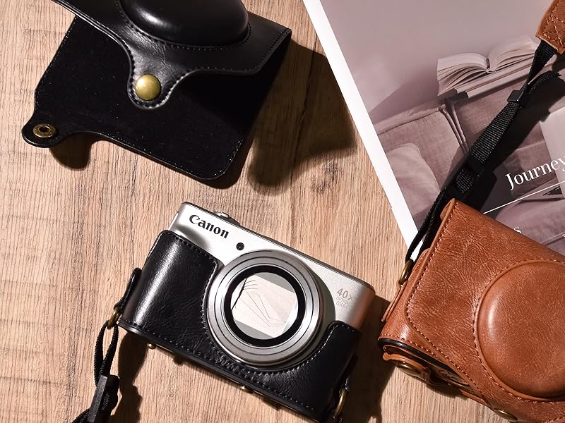 Leather camera cases in black and brown, shown with a compact digital camera, displayed on wooden surface and fabric background.