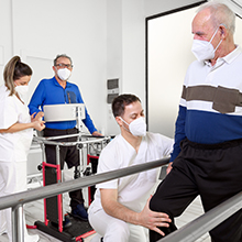 Medical professionals assisting and monitoring someone on physical therapy equipment in a clinical setting.
