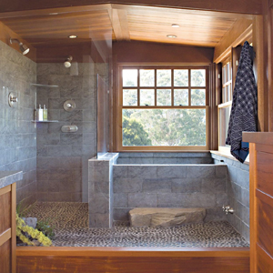 A bathroom with wood walls and ceiling, stone tiles, pebble flooring, and a frameless glass shower.