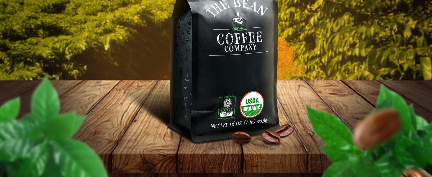 Bag of The Bean Coffee Company organic coffee on wooden surface with coffee beans and greenery.